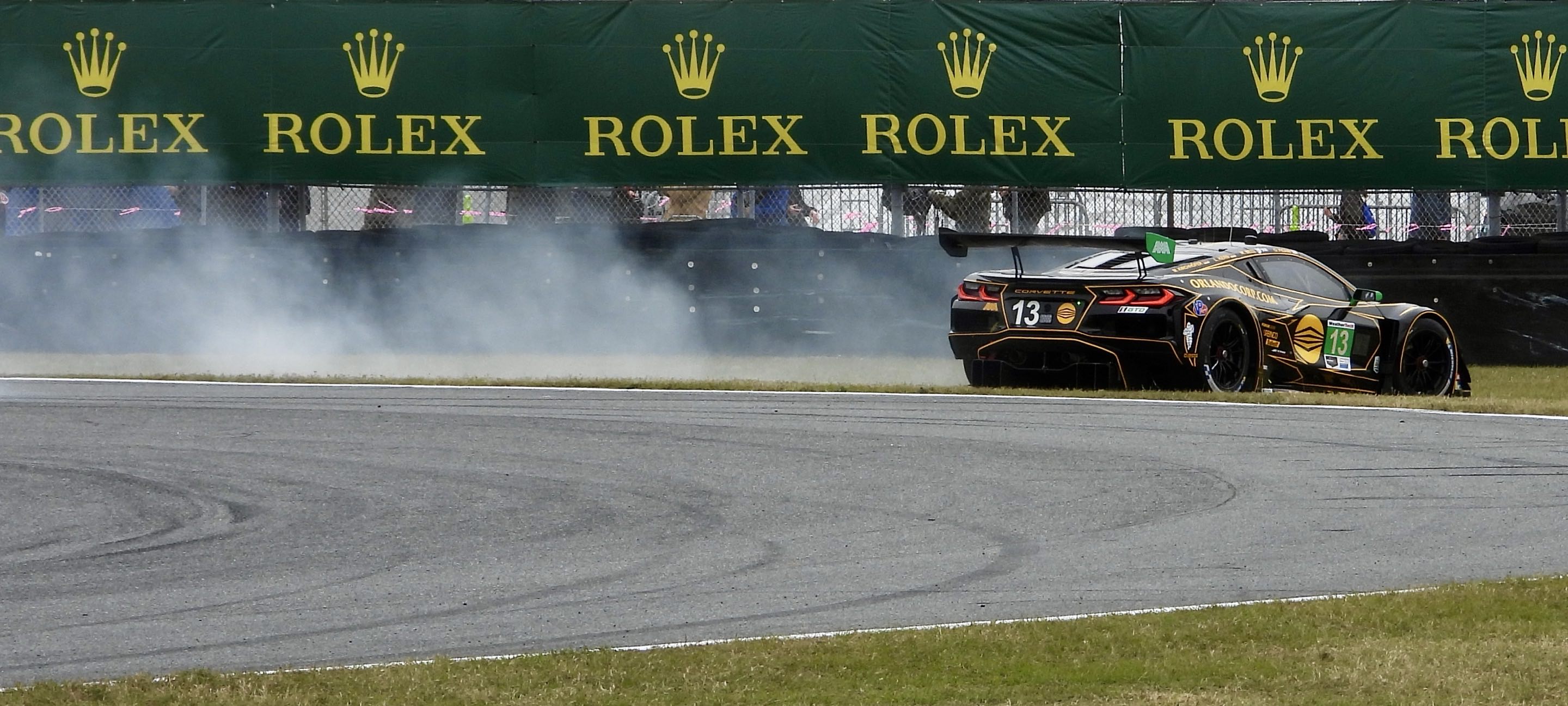 A Corvette GT3 sliding off a race track with smoke trailing behind it